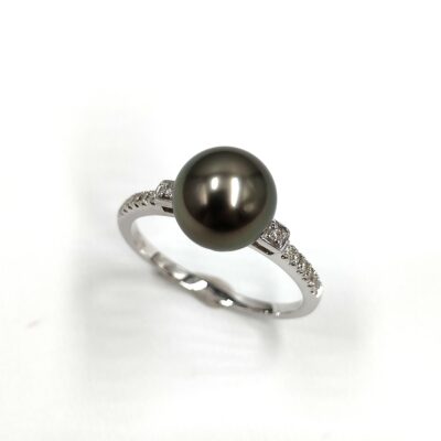 une bague en or blanc ornée d'une perle noire de Tahiti et de diamants. La perle est ronde et de couleur noire profonde, avec une surface lisse et brillante. Elle est sertie au centre de la bague, et encadrée par de petits diamants sertis sur une fine bande en or blanc. La bague est simple et élégante, mettant en valeur la beauté de la perle noire.