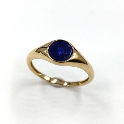une chevalière en or jaune sertie d'une pierre ronde de lapis-lazuli bleu foncé. La monture est simple et élégante, de forme ovale légèrement bombée. La pierre est bien centrée et de bonne qualité. L'ensemble est sobre et raffiné.