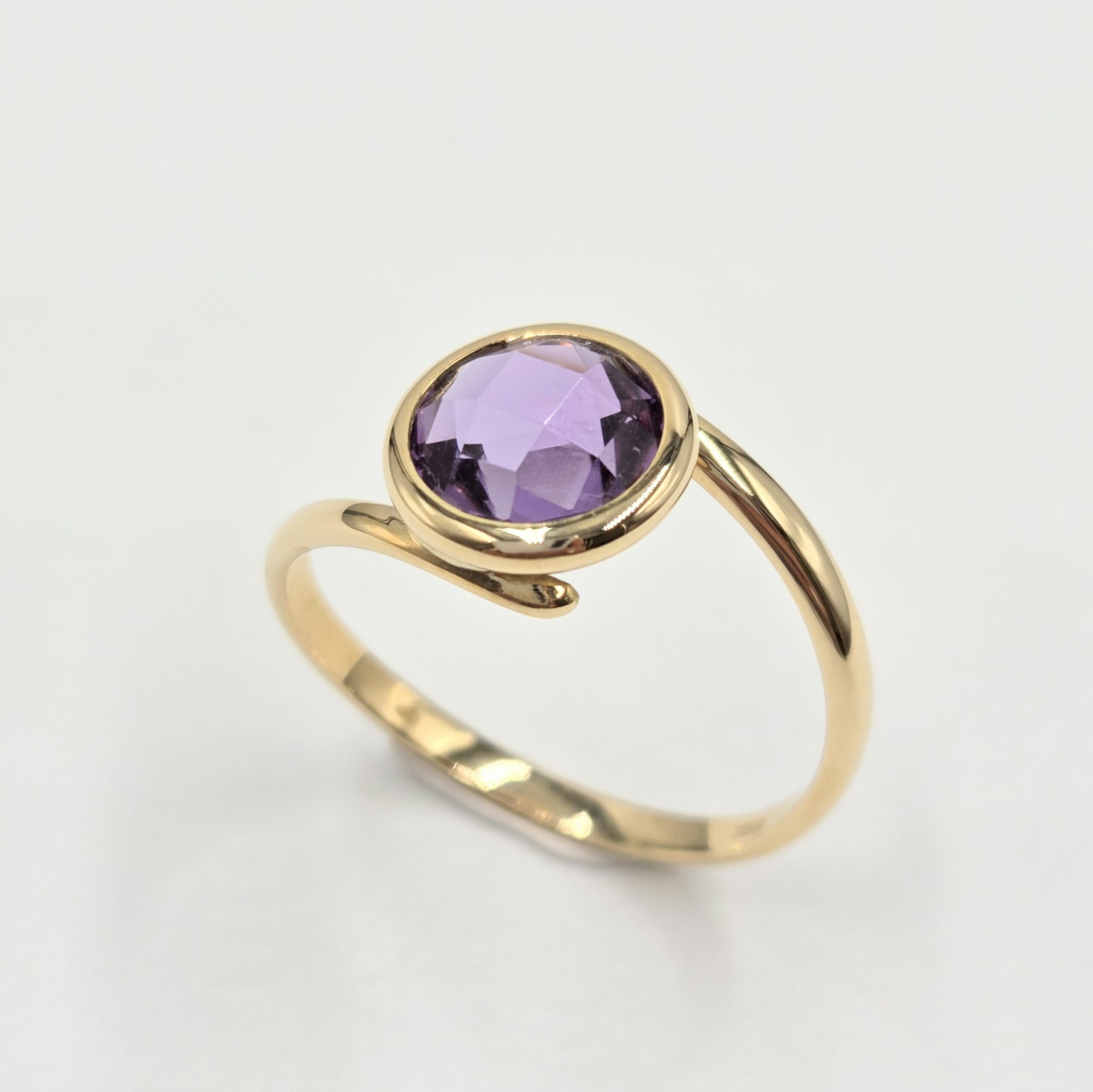 Bague en or jaune avec améthyste violette, ronde sertie clos sur anneau ouvert minimaliste.