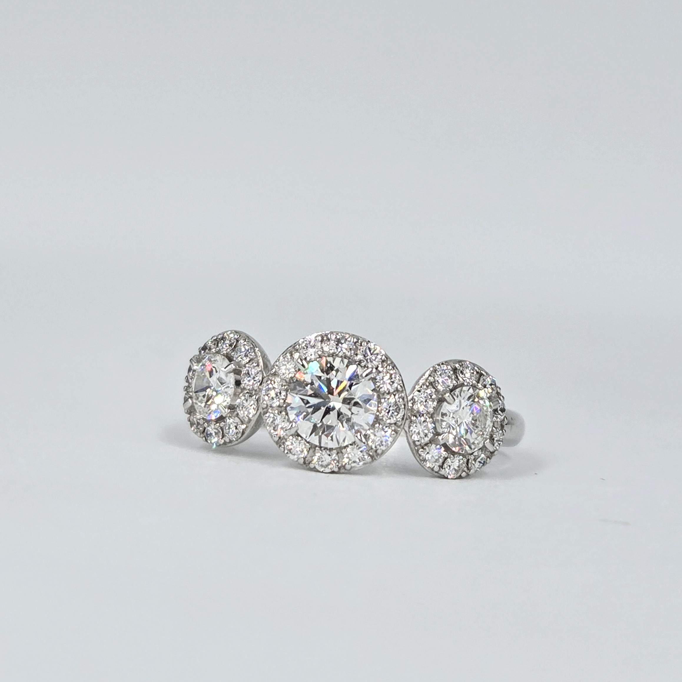 Bague trilogie en or blanc avec trois diamants ronds entourés de halos pavés.
