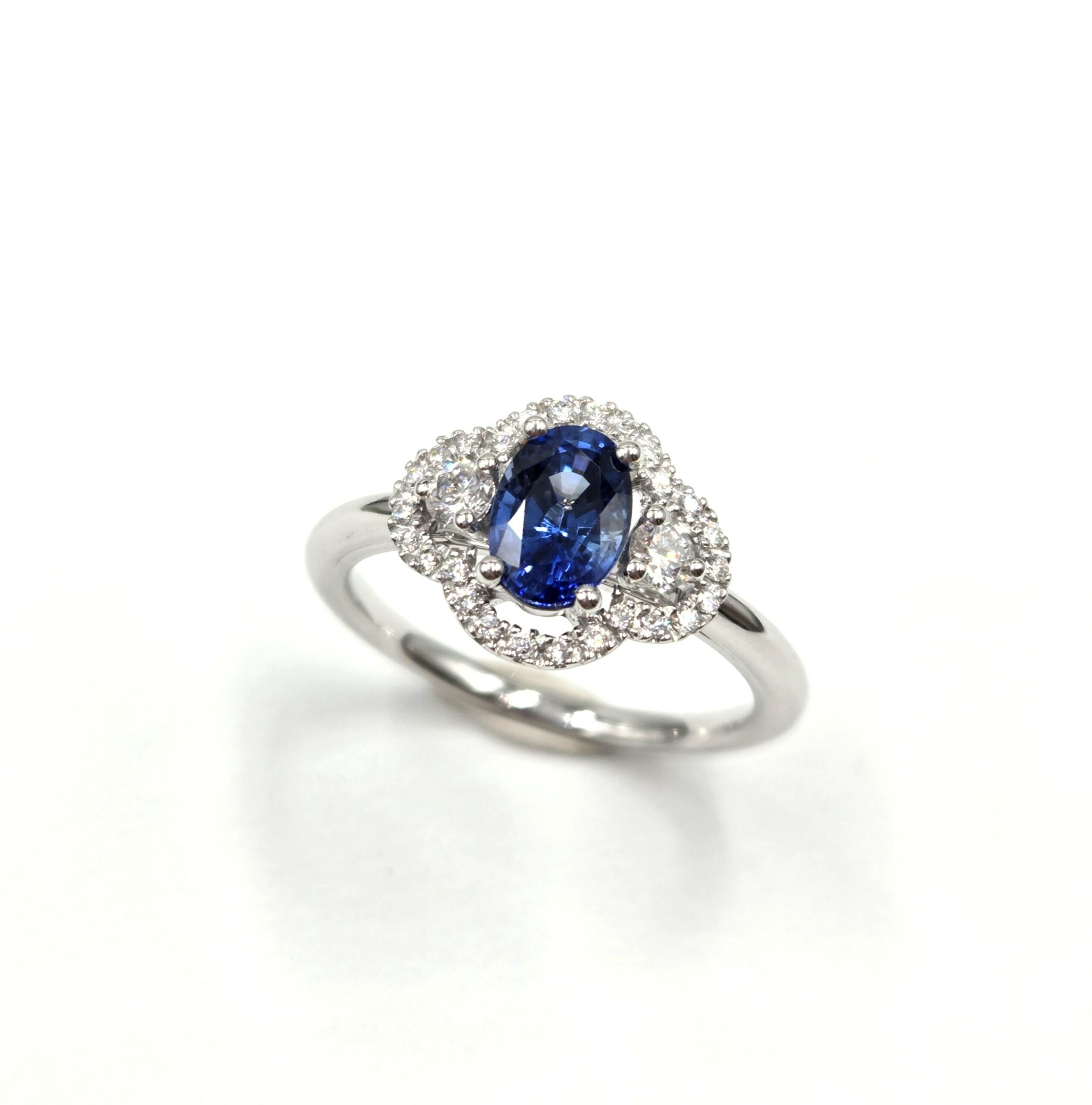 Bague en or blanc avec saphir ovale et halo de diamants en double courbe.