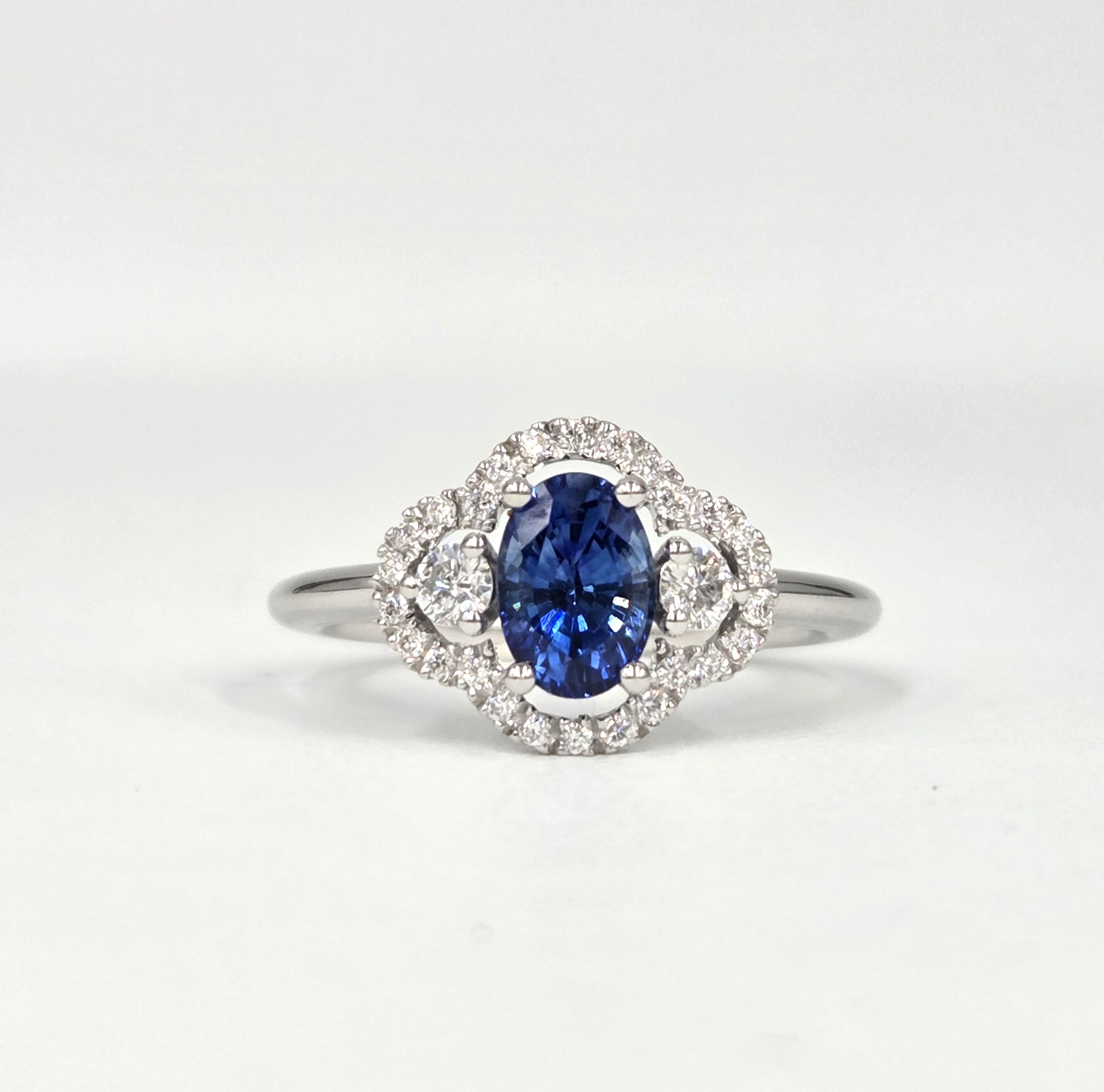 Bague en or blanc avec saphir ovale et halo de diamants en double courbe.