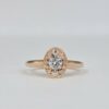 bague en or rose avec diamant rond central et halo ovale pavé de diamants