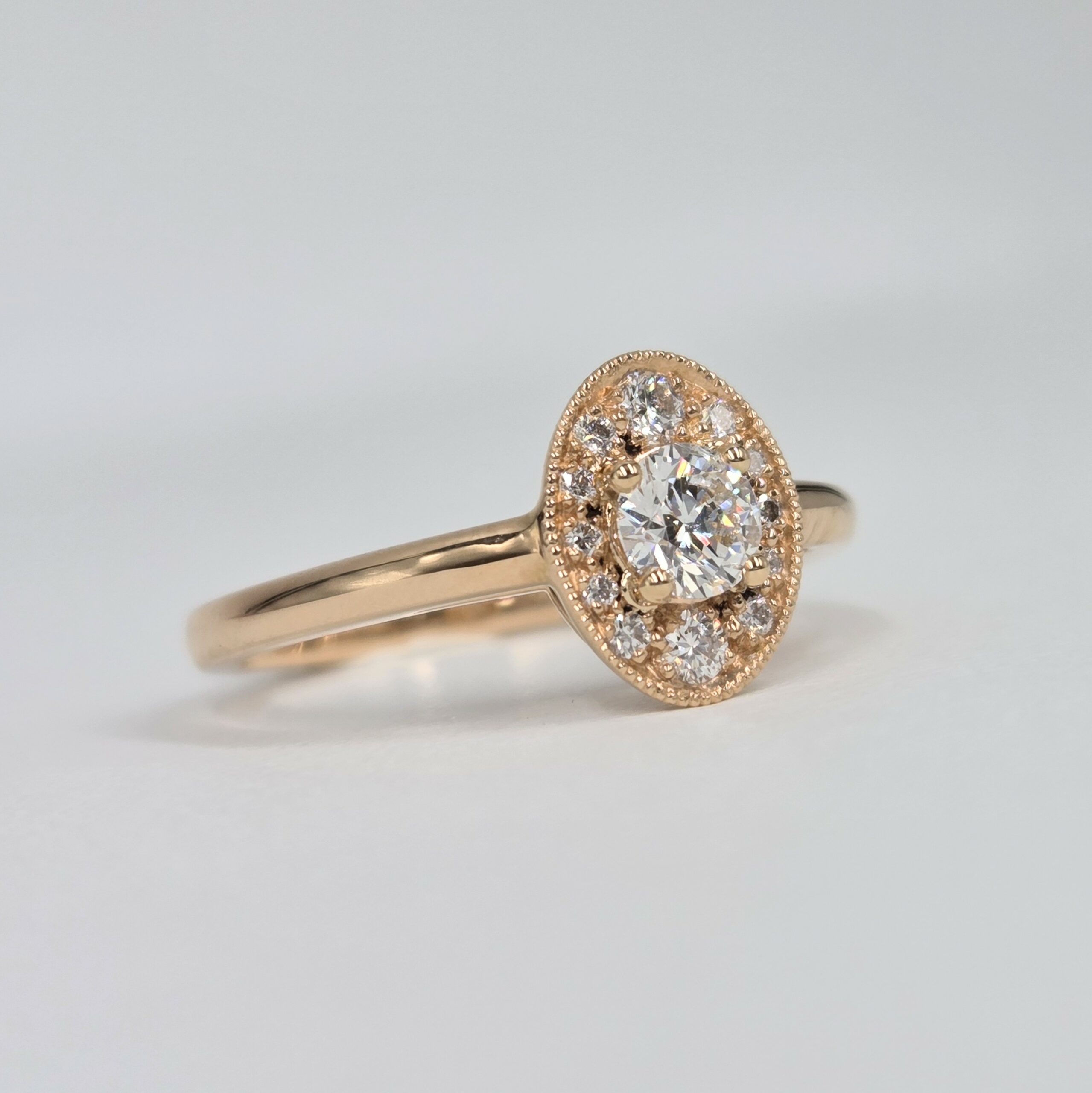 bague en or rose avec diamant rond central et halo ovale pavé de diamants