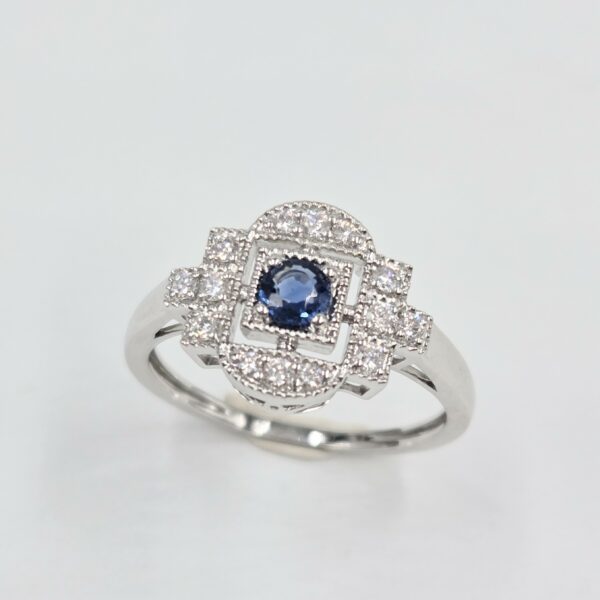 Bague en or blanc palladié avec saphir bleu rond et pavage de diamants en forme art déco.