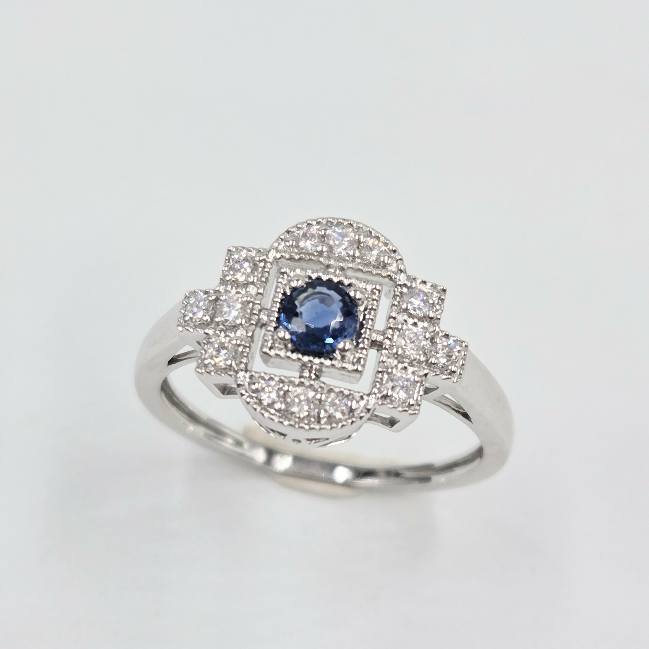 Bague en or blanc palladié avec saphir bleu rond et pavage de diamants en forme art déco.